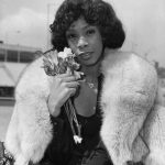 black and white portrait of donna summer wearing a fur stole and holding flowers near her face