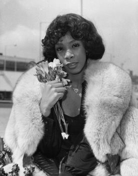 black and white portrait of donna summer wearing a fur stole and holding flowers near her face