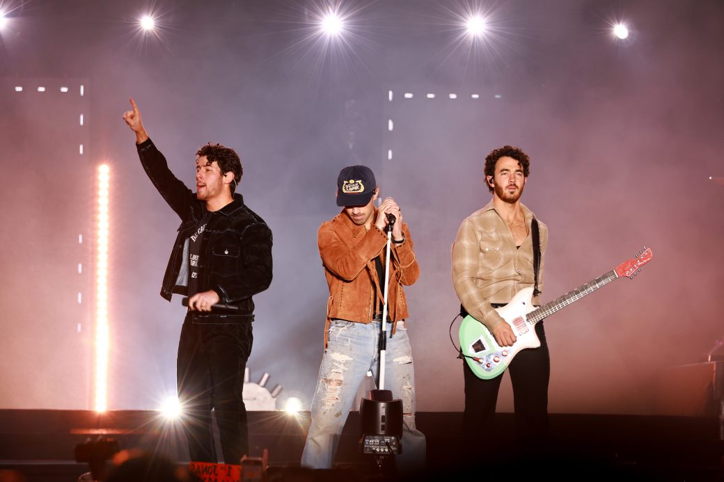 the jonas brothers perform, nick behind the mic and kevin on the guitar, joe is just raising his fist in solidarity