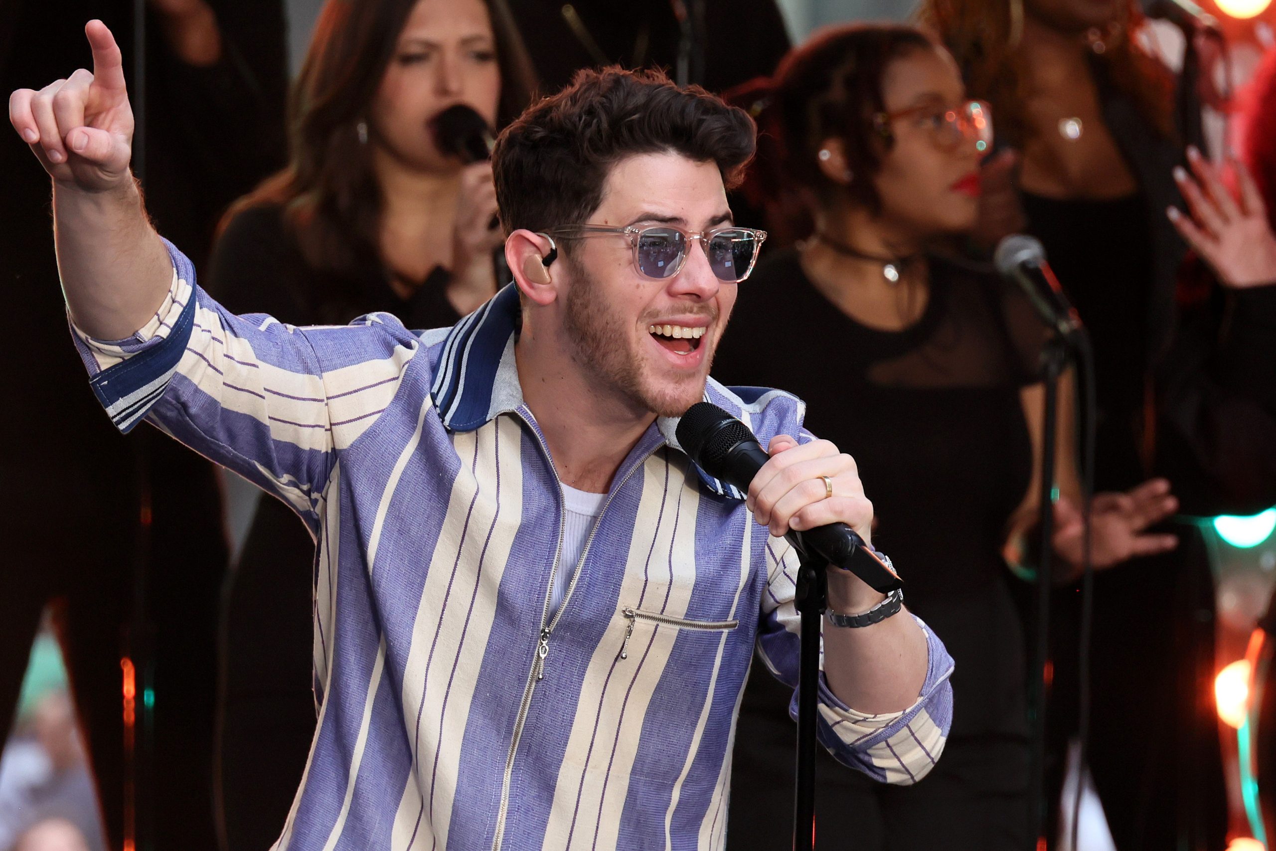 Nick Jonas wears purple sunglasses and a matching striped shirt as he performs