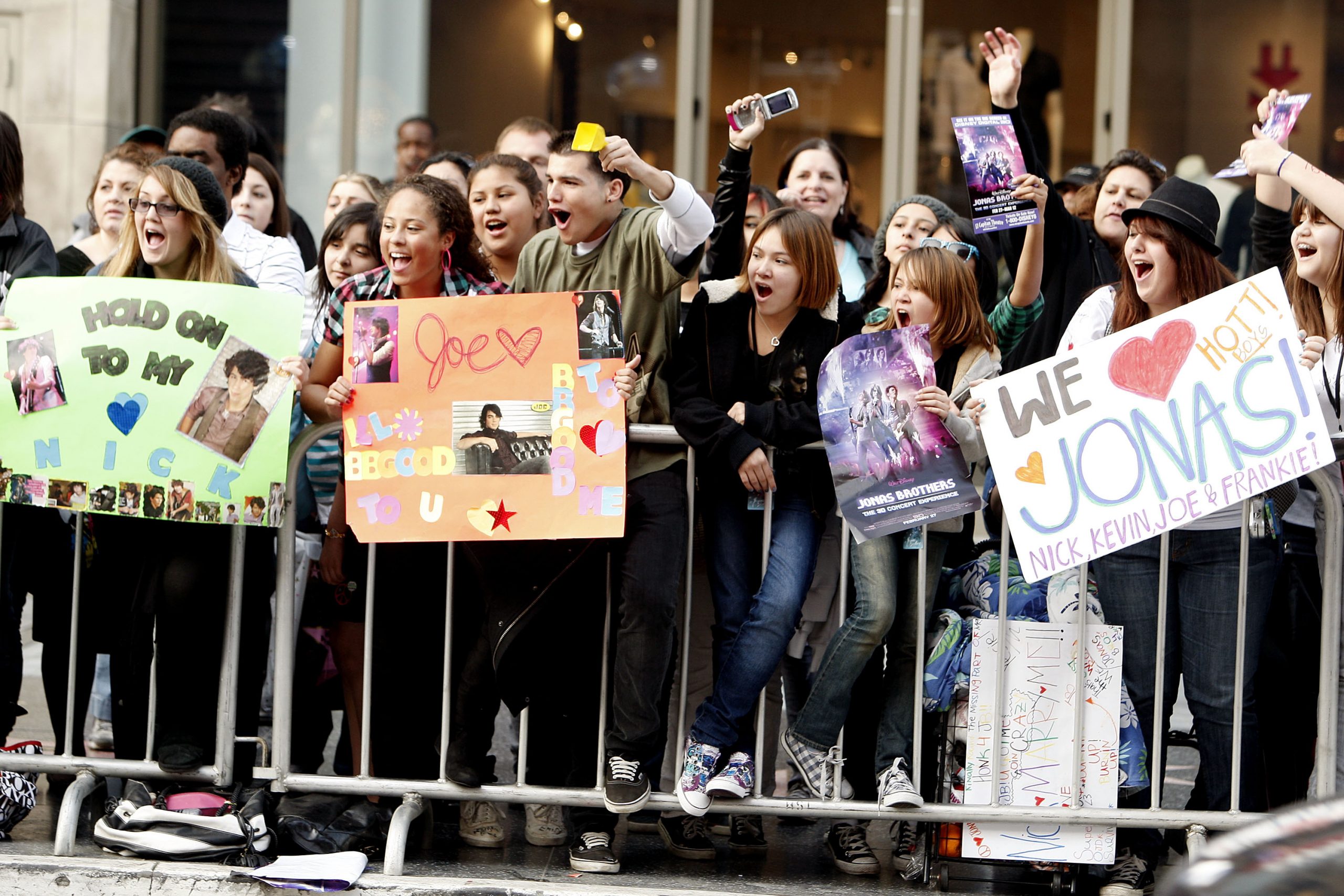 fans stand behind a fence with their jonas brothers signs